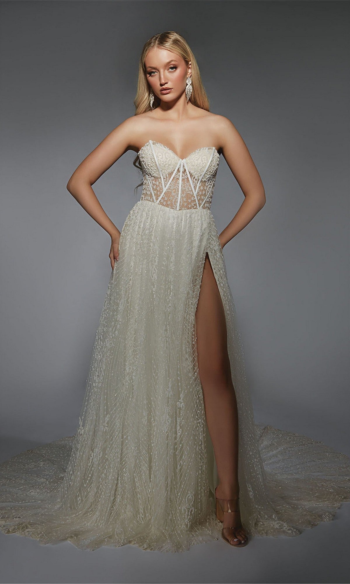 A woman models the Alyce 7133 long formal dress in ivory, featuring a strapless structured bodice, sheer lace gown, and high leg slit, standing against a plain gray background.